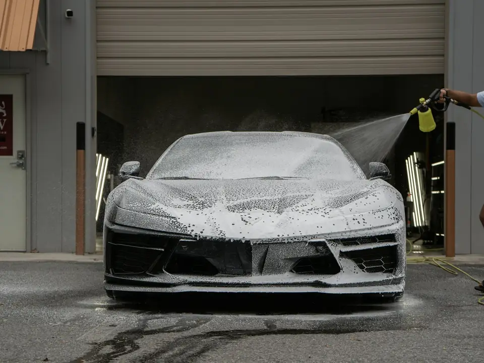 Sports car covered in white snow foam being sprayed during a wash