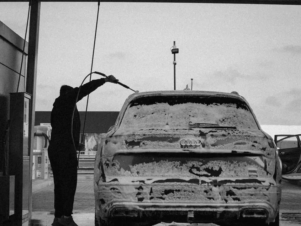 Black and white photo of a person pressure-washing a foam-covered car