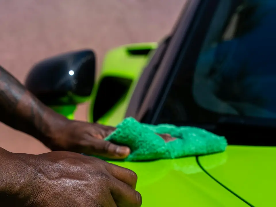 Hands buffing a bright green car with a microfibre cloth