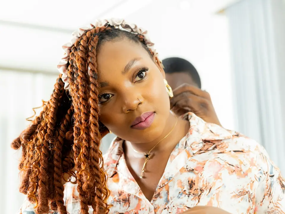 Stylist working on a client's long copper twist braids in a bright salon